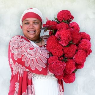 A Baker Creek employee smiles as she holds up a giant bouquet of Higyoku Red Stem Celosia blooms.