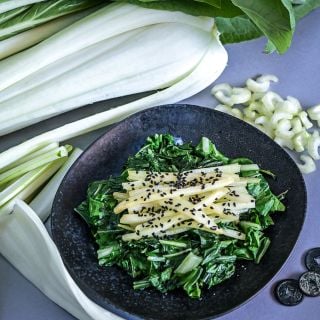 Plated sauteed stems on a bed of greens with black sesame seeds using Snow White Bok Choy.