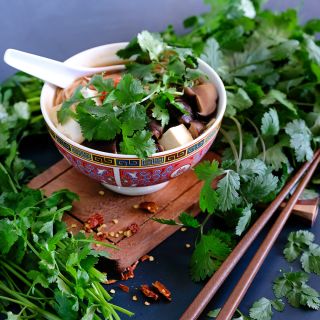 Slo-Bolt Cilantro leaves in a bowl of tofu mushroom soup on a small wooden cutting board.