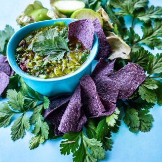 Slo-Bolt Cilantro leaves in green salsa in ablue bowl with purple chips.