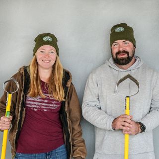 A couple of Baker Creek managers wearing the Baker Creek Logo Beanie and holding garden tools.