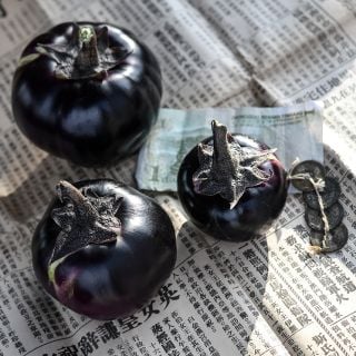 A trio of Qi Ye Round Eggplants on a Chinese newspaper with money and coins.