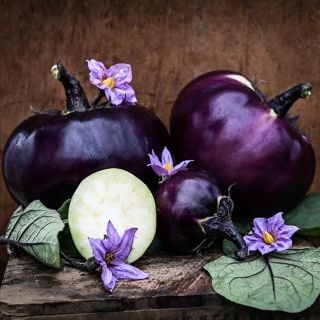 Whole and cut Qi Ye Round Eggplants with purple blooms and red veined leaves on wood.