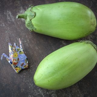 Shiromaru Eggplant on wooden table next to origami bird.