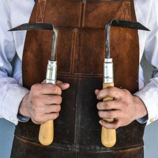 The Baker Creek blacksmith wearing his apron and holding the hand-forged Cape Cod Right and Left Handed Weeders. 