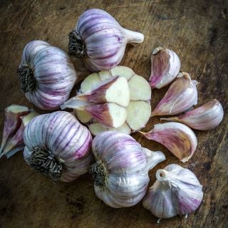 An arrangement of cut and whole Persian Star Garlic bulbs and cloves on a wooden background.