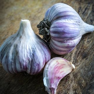 A couple of whole Persian Star Garlic bulbs with a clove on a wood cutting board.