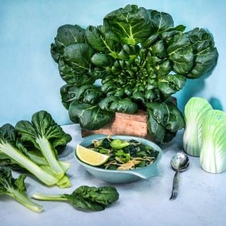 Tatsoi soup with leaves and head of tatsoi on a blue background.
