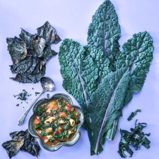 Dazzling Blue Kale leaves alongside a bowl of pasta soup made with kale.