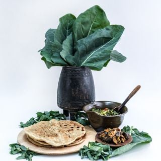 An African vase filled with Sahara Kale beside a bowl of cooked kale and some flatbread. 
