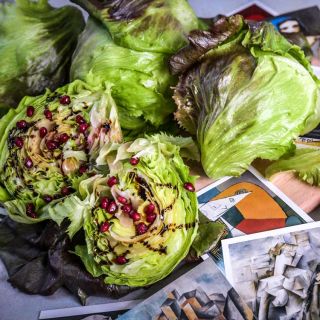 Three heads of Pablo Lettuce with one cut in half covered in dressing and pomegranate pearls.