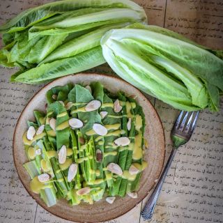 Yedikule Lettuce salad greens in a bowl with dressing, head, and loose leaves on foreign newspaper