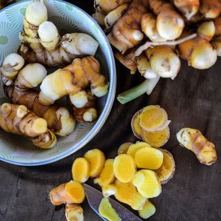 Yellow Turmeric roots with cut roots on a wooden cutting board.