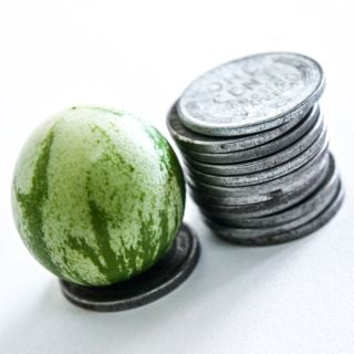 An extreme close-up of a single Tzimbalo Melon Pear beside a stack of pennies on white.