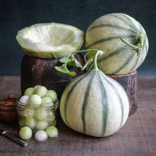 Haru Madhu Melons, whole, halved and in balls on wooden table top and dark background.