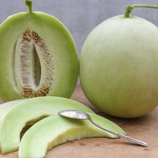 White Lanzhou Melons whole, halved and cut on a wooden board.