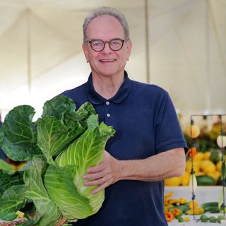 A speaker smiles while holding a large cabbage at the Baker Creek Fall Harvest Festival.