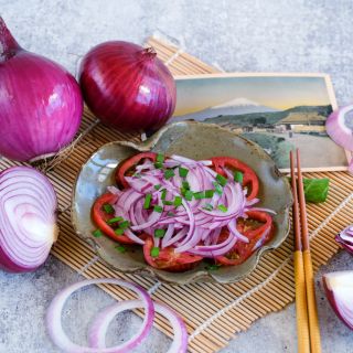 Whole and sliced Akatama Salad Red Onions with an onion tomato salad on a bamboo placemat.