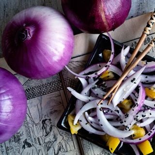 Close-up of whole Akatama Salad Red Onions with a plated onion salad and chopsticks.