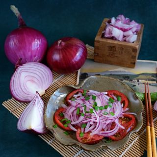 Whole and cut Akatama Salad Red Onions with a tomato onion salad onions in wooden box on a jade background.