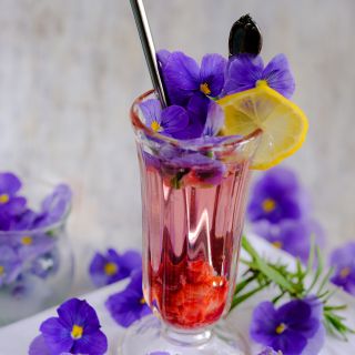 Blue Perfection Violas used as garnish for red drink. against a wooden background.