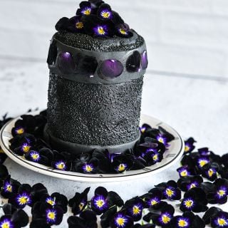 A black fondant cake surrounded by Bowles Black Violas on a light background.