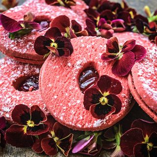 A bunch of Arkwright Ruby Viola Pansy with some red velvet cakes on a wood board.             