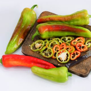 Whole and sliced Giant Aconcagua Sweet Peppers on wooden cutting board with a knife.