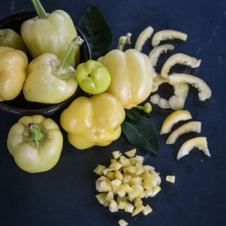 Sliced diced and whole Albino Bullnose Sweet Peppers, some in a bowl on a blue background.