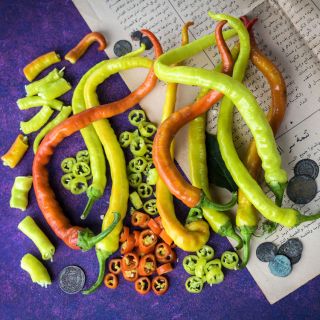A bunch of orange, yellow, and light green Corbaci Peppers next to some chopped peppers and rings on top of an Asian document and coins.