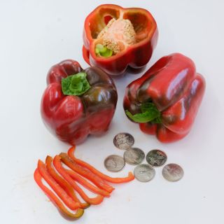 Three King of the North Sweet Peppers, one with its top cut off next to long pepper slices and coins on a white background.