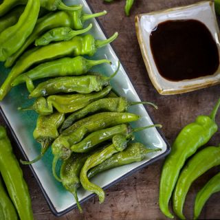 Manganji Sweet Peppers with roasted and some fresh peppers next to a bowl of soy sauce on a wooden background. 