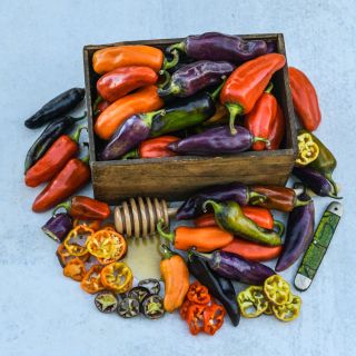 A wooden box full of Pippins Golden Honey Sweet Peppers with a honey dipper covered in honey. Whole and sliced peppers around the box next to a folded pocket knife.