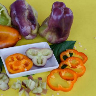 Blot Sweet Peppers with orange to brown shades and one with purple to light green shades. Slices of pepper in a small square dish on the side.