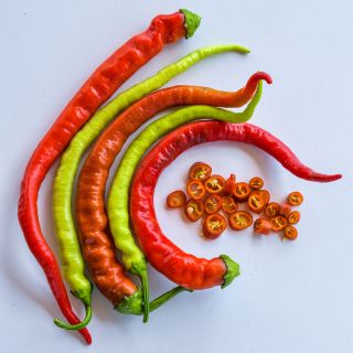 A bunch of orange, red, and light green Corbaci Peppers next to some chopped pepper rings on a white background.