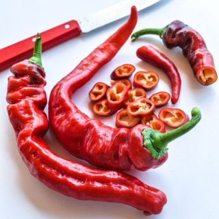 Several red  Jimmy Nardello Italian Peppers with some pepper rings and a red-handled knife in the background.