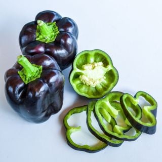 Two Purple Beauty Peppers next to slices on a light background. 