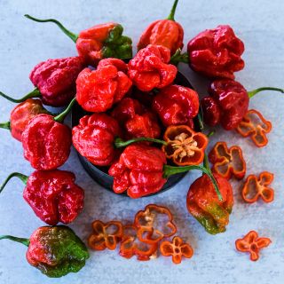 Whole and sliced Moruga Sweet Peppers at various stages of maturity on a light grey background.