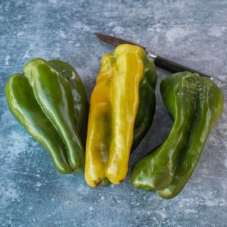 Wooden box of Yellow Monster Peppers in shades of green to greenish-yellow next to a knife on a blue stone textured background.