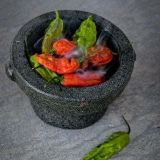 Bhut Jolokia Red in small bowl with steam on grey, marbled table top.