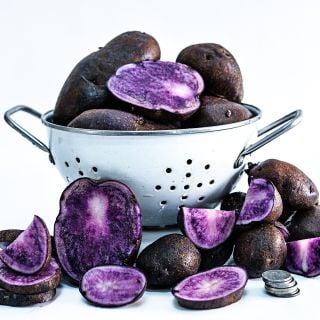 A colander full of Bora Valley mini seed Potatoes surrounded by sliced potatoes.