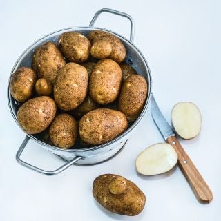 Overhead view of Russet Burbank Potatoes grown from Micro Tubers in a colander and slcied with a knife.