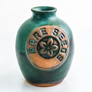 A single greenish blue glazed Handmade Stoneware Pottery Vase with a rareseeds logo on it on white.