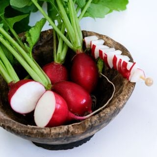 Giant of Sicily Radishes in a wooden bowl with slices on a skewer against a white background.