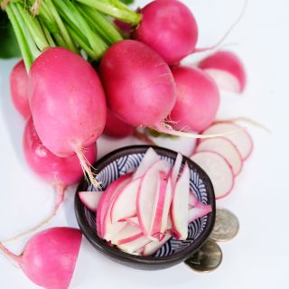 Whole and sliced Pink Dawn Radishes with coins on a white background.