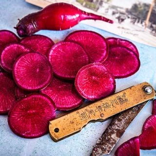 Close-up of Red Beauty Radish slices with a knife on a blue background.