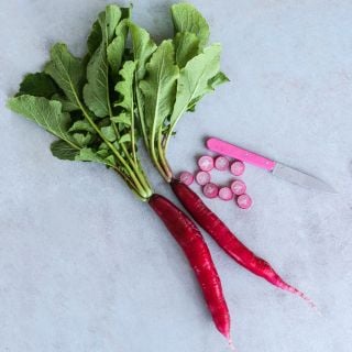 Two Cincinnati Market Radishes with slices and knife on a light blue background.