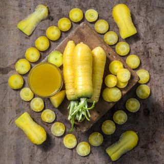 Whole and sliced Uzbek Golden Carrots with carrot juice on a wooden background.
