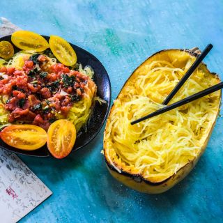 Cooked Kinshi Noodle Winter Squash in the shell and plated with tomato sauce on a blue background.