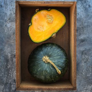 One cut and one whole Buttercup Winter Squash in wooden box on metal background.